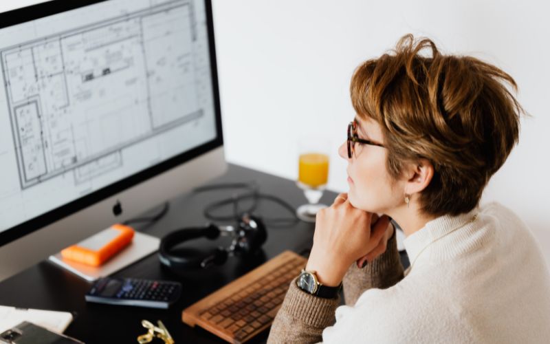 một người phụ nữ ngồi bên bàn làm việc trước màn hình máy tính nói lên vấn đề phân bổ cận thị đối với trẻ ở thành thị cao hơn ở nông thôn